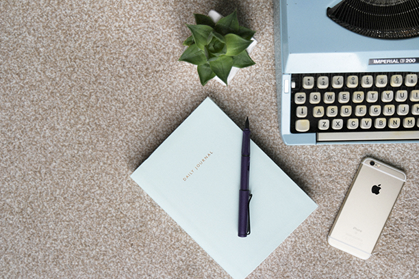 Vintage typewriter with a note book and fountain pen on a cream carpet next to a gold iPhone and a succulent