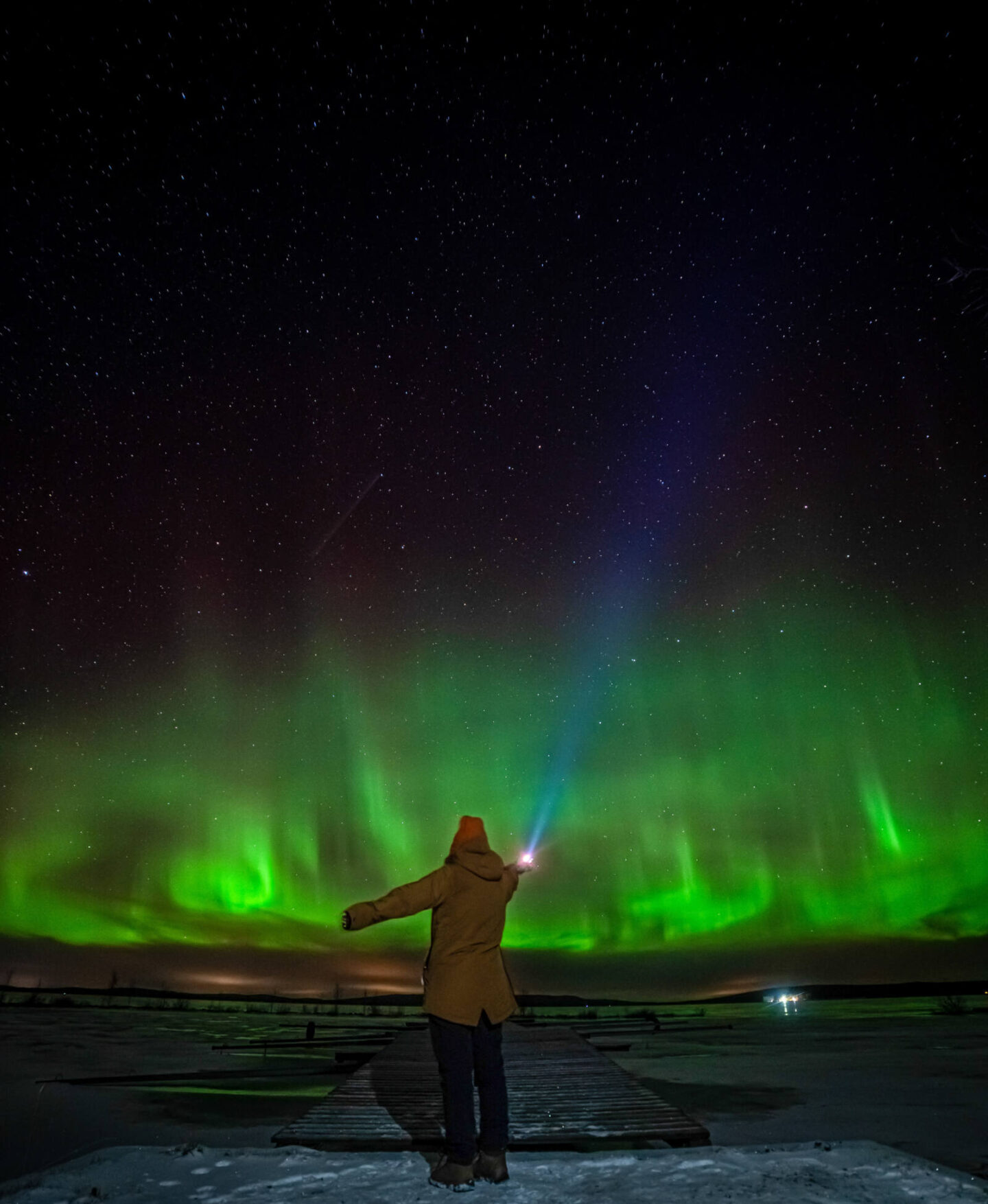 Northern Lights with a woman facing away looking at them while shining a torch